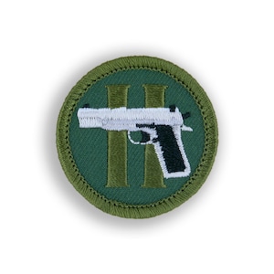 May include: A green embroidered patch with a white handgun and the number "II" in gold thread.