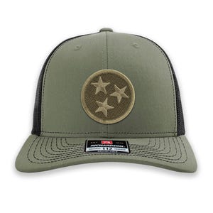 May include: Olive green trucker hat with a black mesh back and a curved brim. The hat features a circular patch with three embroidered stars. The brand name "RICHARDSON" is visible on a tag.