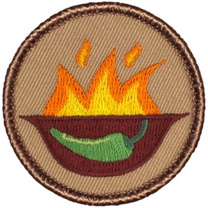 May include: A brown embroidered patch with a green chili pepper on fire. The chili pepper is in a red bowl with flames above it.