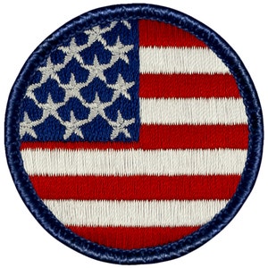 May include: A round embroidered patch featuring the American flag in red, white, and blue. The flag is surrounded by a navy blue border.