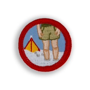 May include: A red, white, and blue embroidered patch with a person standing in front of a yellow tent. The patch is for a camping merit badge.
