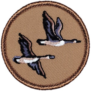 May include: A brown embroidered patch with a beige background featuring two flying geese. The geese are in a V-formation and have white and black markings.