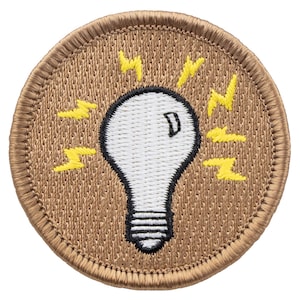 May include: A brown embroidered patch with a white light bulb and yellow lightning bolts around it. The patch has a stitched edge.