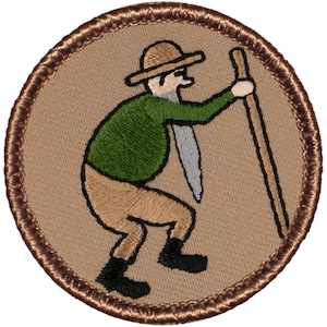May include: A brown embroidered patch with a tan background featuring a cartoon of a man wearing a green shirt, brown pants, and a brown hat. The man is holding a brown stick and has a white beard.
