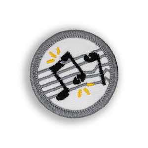 May include: A round, embroidered patch with a white center featuring black musical notes on gray staff lines. The patch has a gray border and yellow starburst accents, perfect for a music enthusiast.