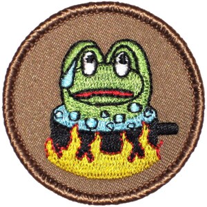 May include: A green frog with a worried expression is being cooked in a pot over a fire. The frog is surrounded by bubbles and the pot is on a yellow flame.