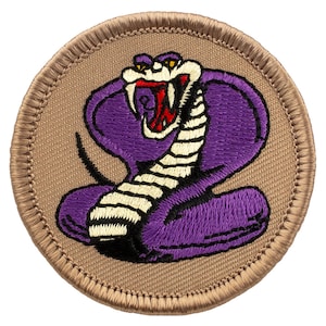May include: Purple embroidered cobra snake patch with a white and black striped pattern on a tan background.