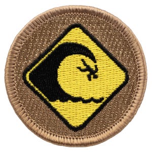 May include: A round, tan embroidered patch with a yellow diamond-shaped warning sign. The sign has a black silhouette of a large wave crashing.