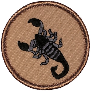 May include: A brown embroidered patch with a black scorpion design. The scorpion is facing right and has a curled tail.