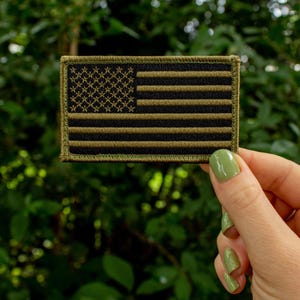 May include: A small, green, embroidered American flag patch with black stars and stripes.