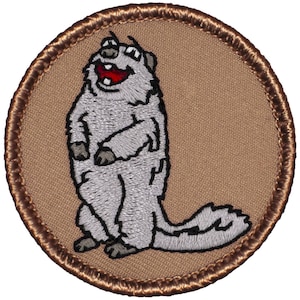 May include: Embroidered patch featuring a cartoon groundhog standing upright with a wide, happy grin. The groundhog is gray with a red mouth and is set against a tan background, framed by a brown stitched border.