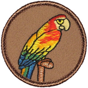 May include: A colorful embroidered patch featuring a parrot perched on a branch. The parrot has red, orange, yellow, green, and blue feathers. The patch is circular and has a brown border.