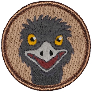May include: Embroidered patch featuring a cartoon ostrich with a brown background and a brown border. The ostrich has a gray head and neck, yellow eyes, a red beak, and a white nose.