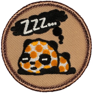 May include: A brown embroidered patch with a white and orange panda bear sleeping with a black cloud above it that says "ZZZ..."