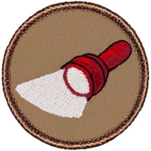 May include: A brown embroidered patch with a white and red flashlight design. The flashlight is pointing to the right.