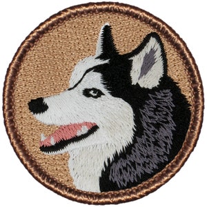 May include: Embroidered patch featuring a black and white husky dog with brown stitching around the edge. The dog's head is facing right and its mouth is open.