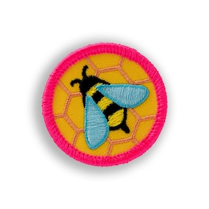 May include: Embroidered patch featuring a yellow honeycomb background with a black and yellow bee and light blue wings. The patch has a bright pink border. This patch is suitable for jackets, bags, or other fabric items.