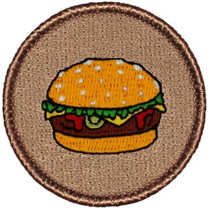 May include: A brown embroidered patch with a cartoon image of a hamburger. The hamburger has a yellow bun, green lettuce, red tomato, and a brown patty.