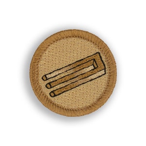 May include: A brown embroidered patch with a beige background featuring a stylized image of a chair. The chair is drawn in black outline with brown shading.