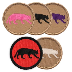 May include: Five embroidered patches featuring a black panther silhouette in various colors. The patches are circular and have a tan background. The panther is pink, black, purple, white, and black on a red background.