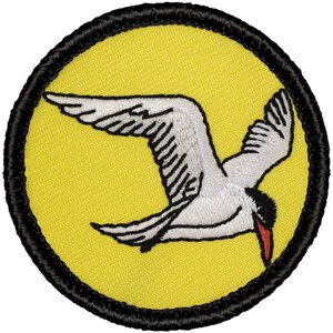 May include: A white embroidered bird with a red beak flying against a yellow background. The bird is surrounded by a black circle.