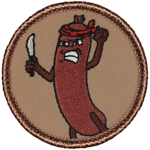 May include: A brown embroidered patch with a cartoon sausage wearing a red bandana and holding a knife. The sausage has a menacing expression and is standing on a tan background.