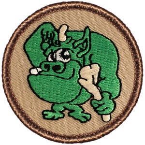 May include: Green embroidered patch with a cartoon goblin holding a stick. The patch is circular and has a brown border.