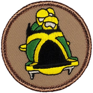 May include: A brown embroidered patch with a yellow and green bobsled with two people inside. The bobsled has black accents and white runners.