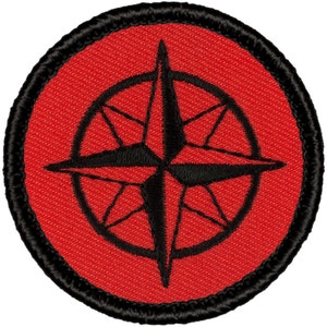 May include: Red embroidered patch with a black compass design. The compass has a star shape with four points and a circle around it.