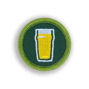 May include: A green embroidered patch with a white outline of a glass of beer. The beer is yellow.