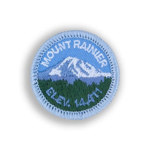 May include: A blue and green embroidered patch with the text "Mount Rainier" and "Elev. 14,410" around a white mountain image.