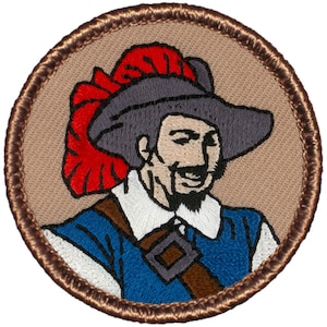 May include: Embroidered patch featuring a cartoon illustration of a man wearing a red and gray hat with a brown sash. The man is smiling and has a beard. The patch is surrounded by a brown border.
