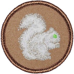 May include: A brown embroidered patch with a white squirrel on a tan background. The squirrel has a green eye.