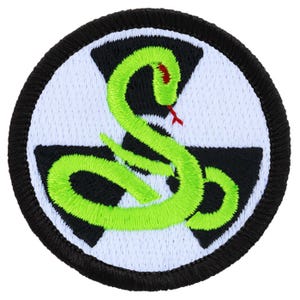 May include: A green snake with a red tongue is coiled around a black and white symbol. The symbol is a stylized version of a radiation symbol. The patch is circular and has a black border.
