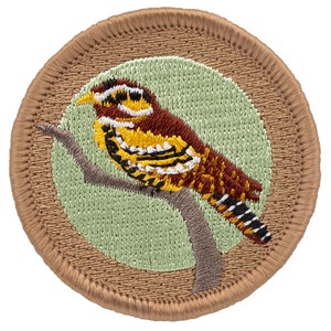 May include: A brown embroidered patch with a green background featuring a yellow, black, and red bird perched on a branch.