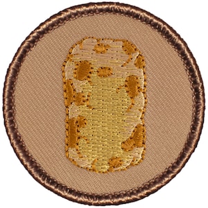 May include: A brown embroidered patch with a tan background. The patch features a tan and brown camouflage pattern in the shape of a potato.