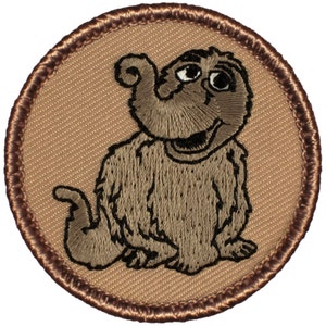 May include: Embroidered brown patch with a cartoon image of a brown furry elephant with a big smile and a curled trunk. The patch is surrounded by a brown stitched border.