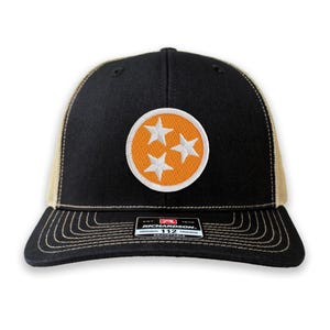 May include: A black and tan trucker hat with an orange circle and three white stars, a patch that says "Richardson 112 Original Trucker Adjustable" is on the front of the hat.