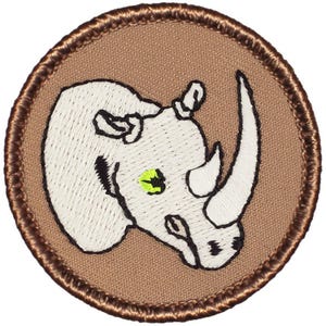 May include: A brown embroidered patch with a white rhinoceros with a green eye. The patch is circular and has a brown border.