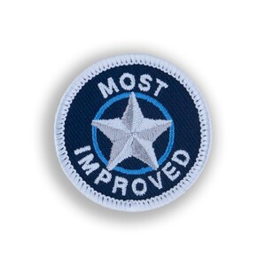 May include: A blue and white embroidered patch with a white star in the center and the words "MOST IMPROVED" around the star.