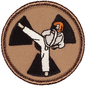 May include: A brown embroidered patch with a white figure performing a karate kick in front of a black and white radiation symbol.