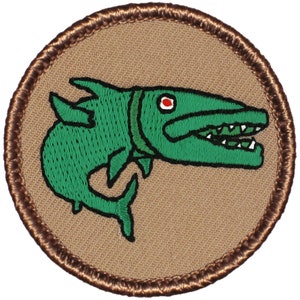 May include: A brown embroidered patch with a green fish with a large mouth and a red eye. The fish is on a tan background.