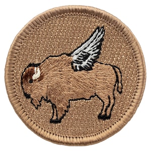May include: A brown embroidered patch with a brown bison with white wings. The patch is circular and has a brown stitched border.