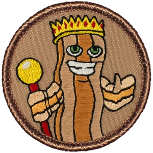 May include: A brown embroidered patch with a cartoon bacon character wearing a gold crown and holding a red and yellow scepter. The bacon character has a smiling face with green eyes and a white smile.