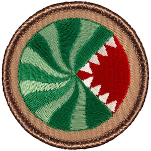 May include: A round, brown embroidered patch with a green and white spiral design. A red mouth with white teeth is partially visible on the right side of the patch.