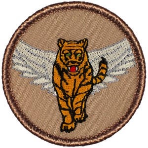 May include: Embroidered patch featuring a brown tiger with white wings, a red mouth, and green eyes. The tiger is standing on a tan background with a brown border.