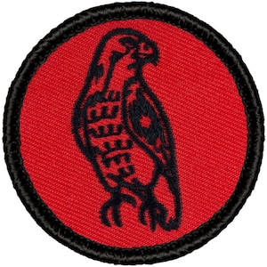 May include: A black embroidered patch with a red background. The patch features a stylized black hawk with a detailed design.
