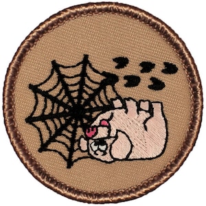 May include: A brown embroidered patch with a pink pig caught in a black spider web. The pig has a pink nose and black eyes. There are three black paw prints above the web.