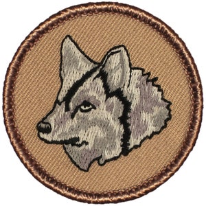 May include: A brown embroidered patch with a gray wolf head design. The wolf is facing left and has a black eye.