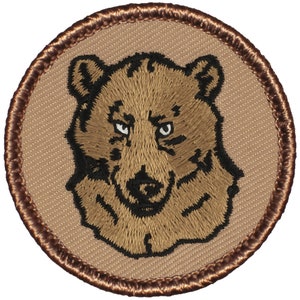 May include: A brown embroidered patch with a brown bear face on a tan background. The bear has black eyes and a black nose.